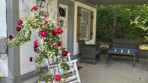 A covered porch with a white rocking chair, a small table, and a potted plant with red flowers.