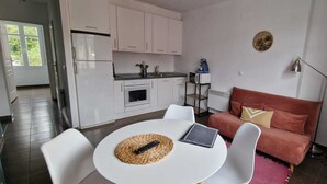 Un espacio habitable compacto con kitchenette, una zona de comedor con mesa y sillas, un sofá y una lámpara.