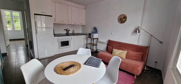 A compact living space with a kitchenette, a dining area with a table and chairs, a sofa, and a lamp.
