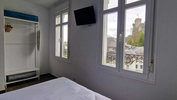 Una habitación con una cama, un televisor instalado en la pared y un ventanal con vistas a edificios.