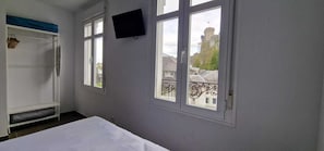 A room with a bed, a TV mounted on the wall, and a window with a view of buildings.