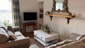 A living room with a television, a white sofa, a coffee table with a plant, and a decorative mirror on the wall. - Berry View - Idyllic cosy cottage on berry farm (Rattray)
