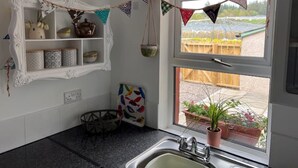 A kitchen with a window, a sink, a decorative shelf, and a hanging light fixture. - Berry View - Idyllic cosy cottage on berry farm (Rattray)