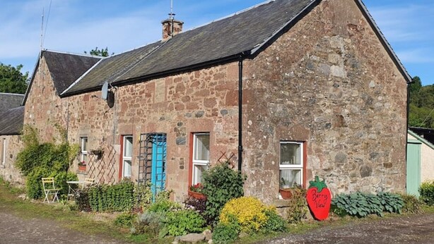 A stone building with a sloped roof, multiple windows, and a small garden area with plants and a red sign. - Berry View - Idyllic cosy cottage on berry farm (Rattray)