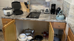 Eine kleine Küche mit einem Herd, einem Slow Cooker, einem Toaster, einem Mixer und einem Wasserkocher.