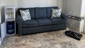 Ein Wohnzimmer mit grauem Sofa, dekorativen Kissen, Deckenventilator, Wasserspender und Stehlampe.