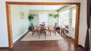 A dining area with a wooden table and chairs, a hanging light fixture, and potted plants.