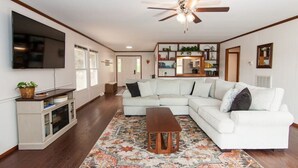A living room with a sectional sofa, a coffee table, a TV mounted on the wall, and a ceiling fan.