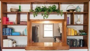 A kitchen area with a wooden island, two stools, and a built-in bookshelf with various items.