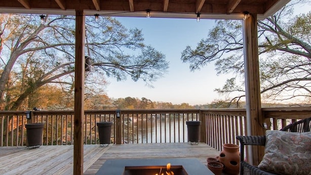 A wooden deck with a fire pit, outdoor furniture, and a view of trees and a body of water.