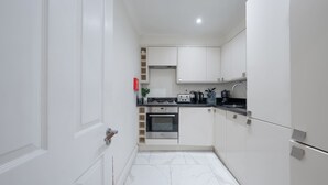 A narrow kitchen with white cabinets, a built-in oven, and a black countertop. - Cozy 2-Bedroom Loft next to Park Lane (London)