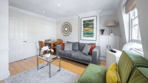 A living room with a grey sofa, a green armchair, a coffee table, and a dining area with a wooden table and chairs. - Cozy 2-Bedroom Loft next to Park Lane (London)