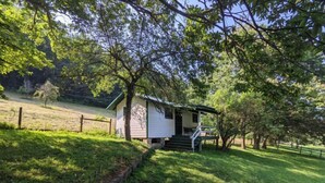 Une petite cabane blanche avec un porche, entourée d’une végétation luxuriante et d’arbres.