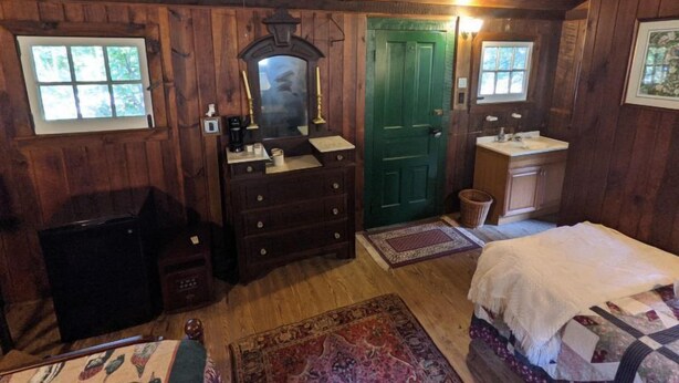 Une chambre à coucher dans une cabane en bois, avec une commode, un miroir, une porte verte, un lavabo et un lit.