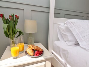 A neatly made bed with white linens, a bedside table with a lamp, a plate of croissants and strawberries, and a glass of orange juice. - Prestella (Filey)