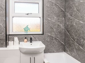 A bathroom with a white sink, a window with a decorative fish, and marble walls. - Prestella (Filey)