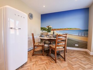 A dining area with a herringbone wooden floor, a white refrigerator, a dining table with chairs, and a mural of a beach scene on the wall. - Prestella (Filey)