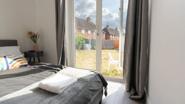 A bedroom with a bed, a nightstand, a vase with flowers, and a view of the outside through a sliding door.