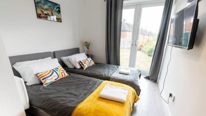 A bedroom with two beds, a gray headboard, a yellow blanket on one bed, and a painting on the wall.