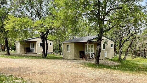Two small, single-story cabins with attached porches, surrounded by trees and a gravel driveway. - Chalet Nature - Lodges du Bois Dodo (Septfonds)