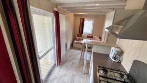 A compact kitchen with a gas stove, a small table, and a window with curtains. - Chalet Nature - Lodges du Bois Dodo (Septfonds)