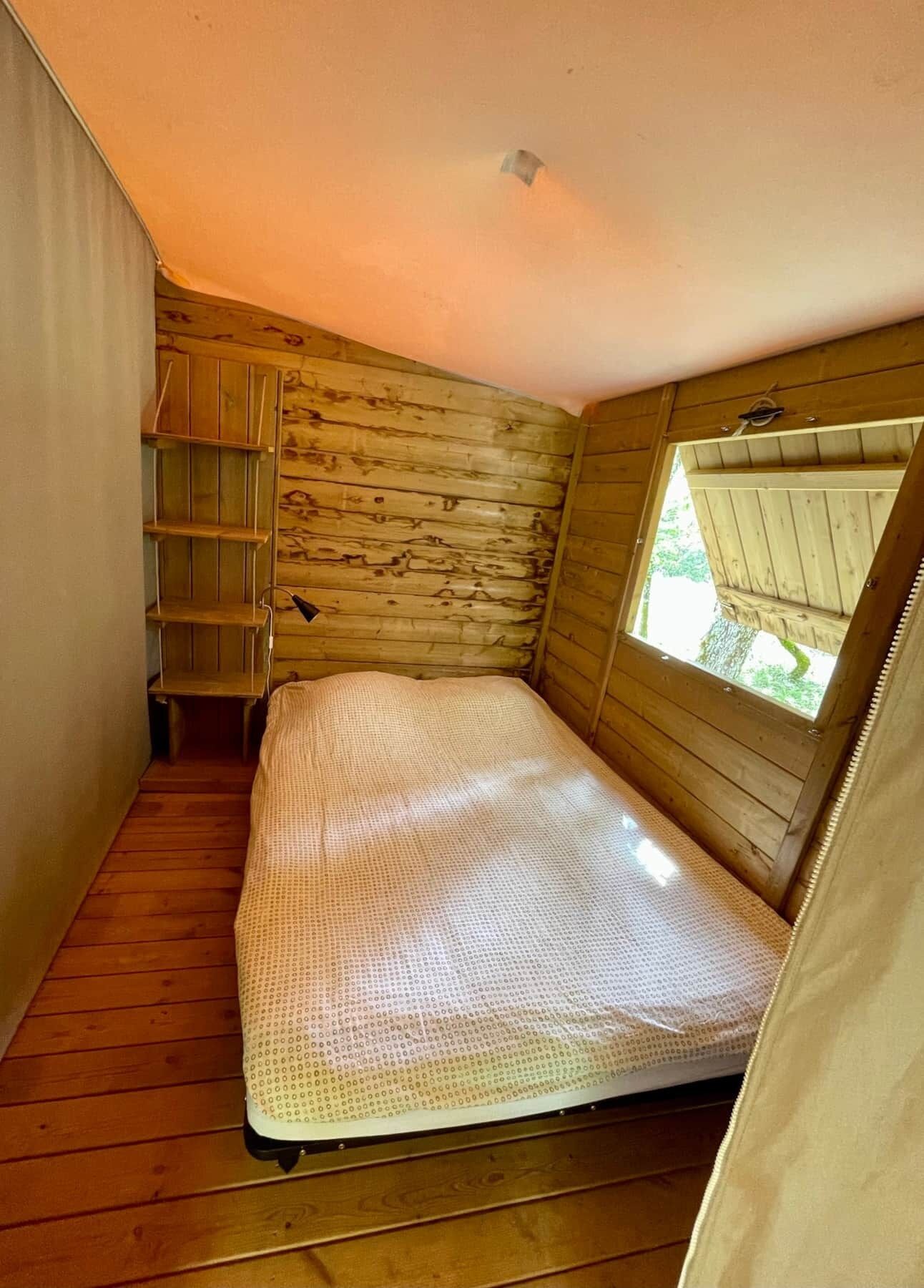 Una habitación pequeña de madera con una cama litera, un estante y una ventana.