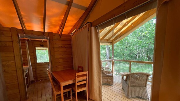 Eine Holzhütte mit Holztisch und -stühlen, einem Fenster und einem Balkon mit Korbstühlen.