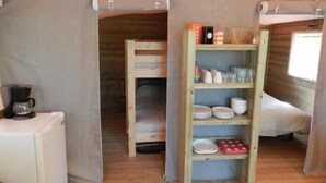Une cabane chaleureuse avec un lit en mezzanine, une petite kitchenette et une étagère où sont rangés la vaisselle et les verres.