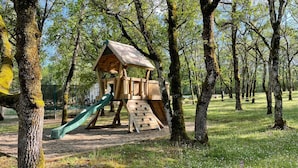 Une structure de jeux en bois, avec un toboggan et un mur d’escalade, installée dans un parc.