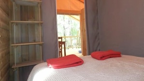 Une chambre avec un lit, deux serviettes rouges, une étagère en bois et une vue sur l’extérieur par une porte.