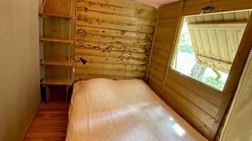 Een kleine, houten kamer met een stapelbed, een plankenwand en een raam.
