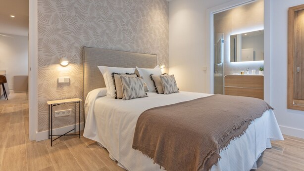 A bedroom with a large bed, a bedside table, a nightstand, a mirror, and a wooden door. - Charming 2-Bed Apartment in Conde Duque, Madrid (Madrid)