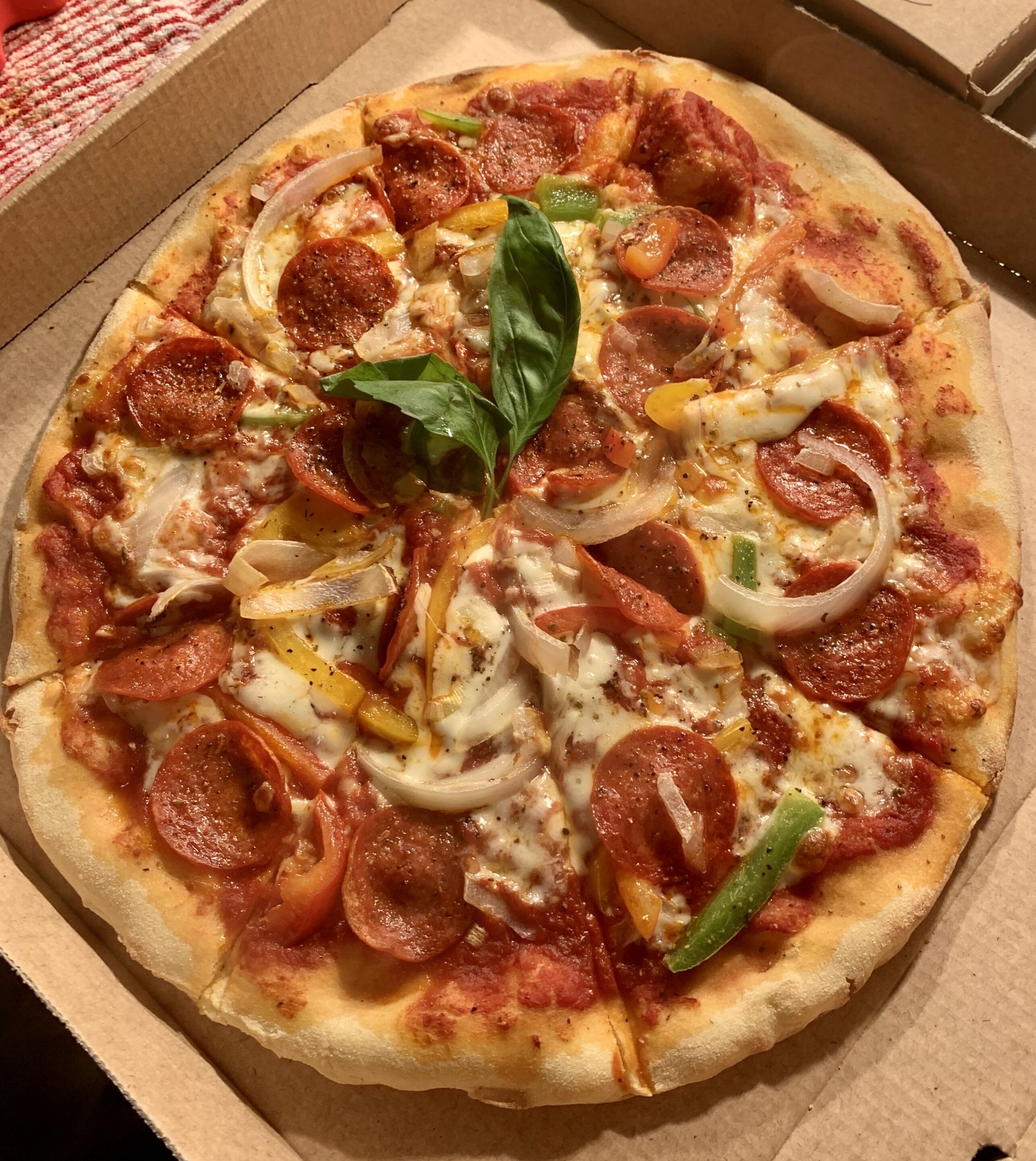 A pizza with pepperoni, onions, and green peppers in a cardboard box.