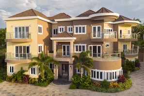 A multi-story residential building with balconies, a central entrance, and surrounding landscaping.