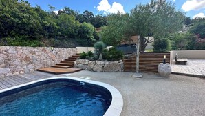 Una piscina con muro de piedra, terraza de madera y una escalera de piedra que conduce a una casa.