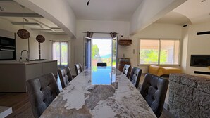 Un comedor amplio con una mesa larga, sillas de cuero, una cocina con horno empotrado y vistas al exterior a través de un ventanal grande.