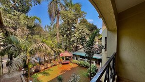 A courtyard with a swing set, palm trees, and a small building with a red roof. - Rajdhani Resort Lonavala (Mawal)