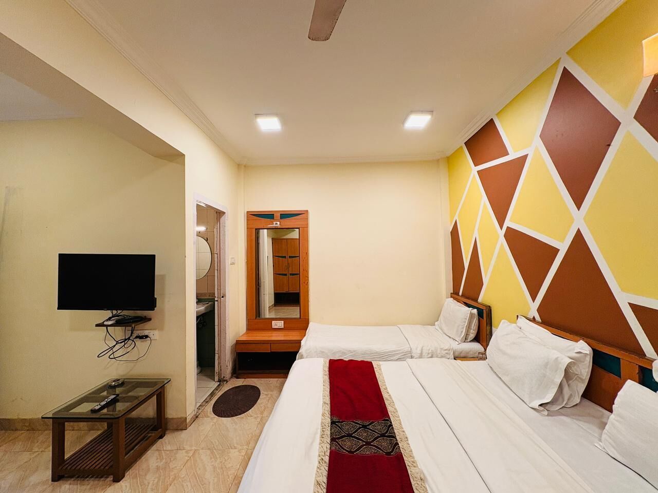 A hotel room with two beds, a television, and a mirror.