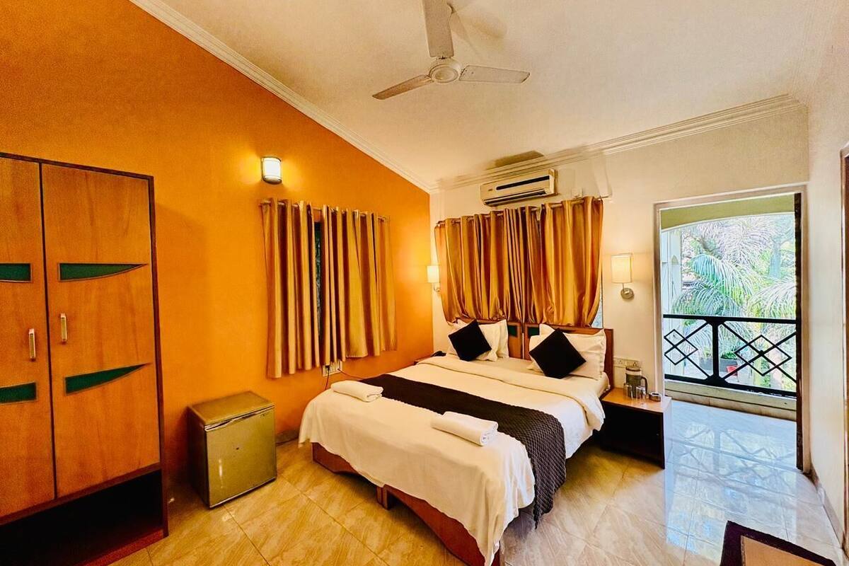 A hotel room with a bed, a wardrobe, a bedside table, a lamp, and a view of the outdoors.