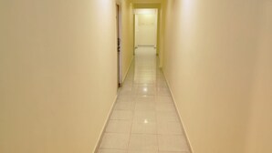 A narrow, well-lit hallway with a tiled floor leading to a door at the end. - Rajdhani Resort Lonavala (Mawal)