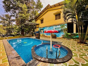 A swimming pool with a circular hot tub, surrounded by a patterned tile floor and a mural of a beach scene. - Rajdhani Resort Lonavala (Mawal)