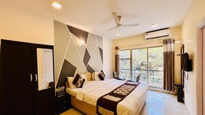 A modern hotel room with a large bed, a wardrobe, a flat-screen TV, and a balcony with a view of trees. - Rajdhani Resort Lonavala (Mawal)