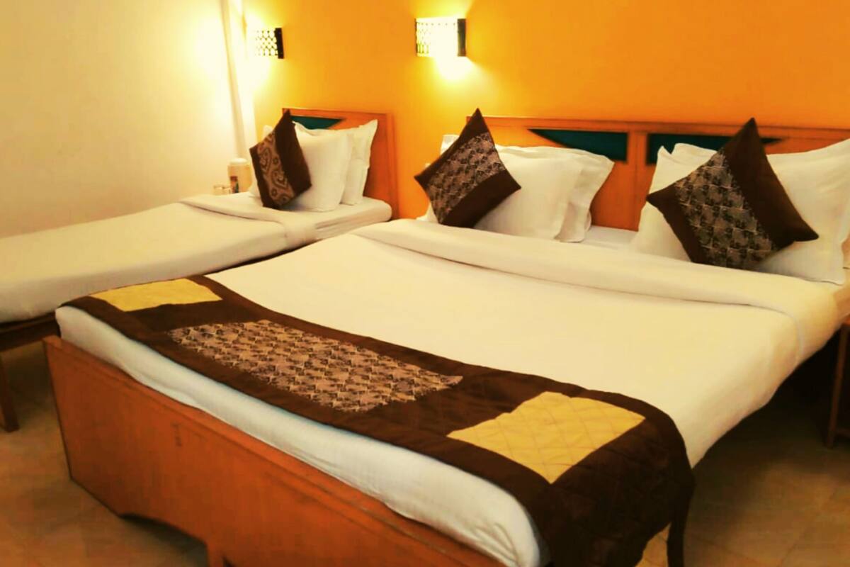 A hotel room with two single beds, each with a wooden headboard, white linens, and patterned pillows.