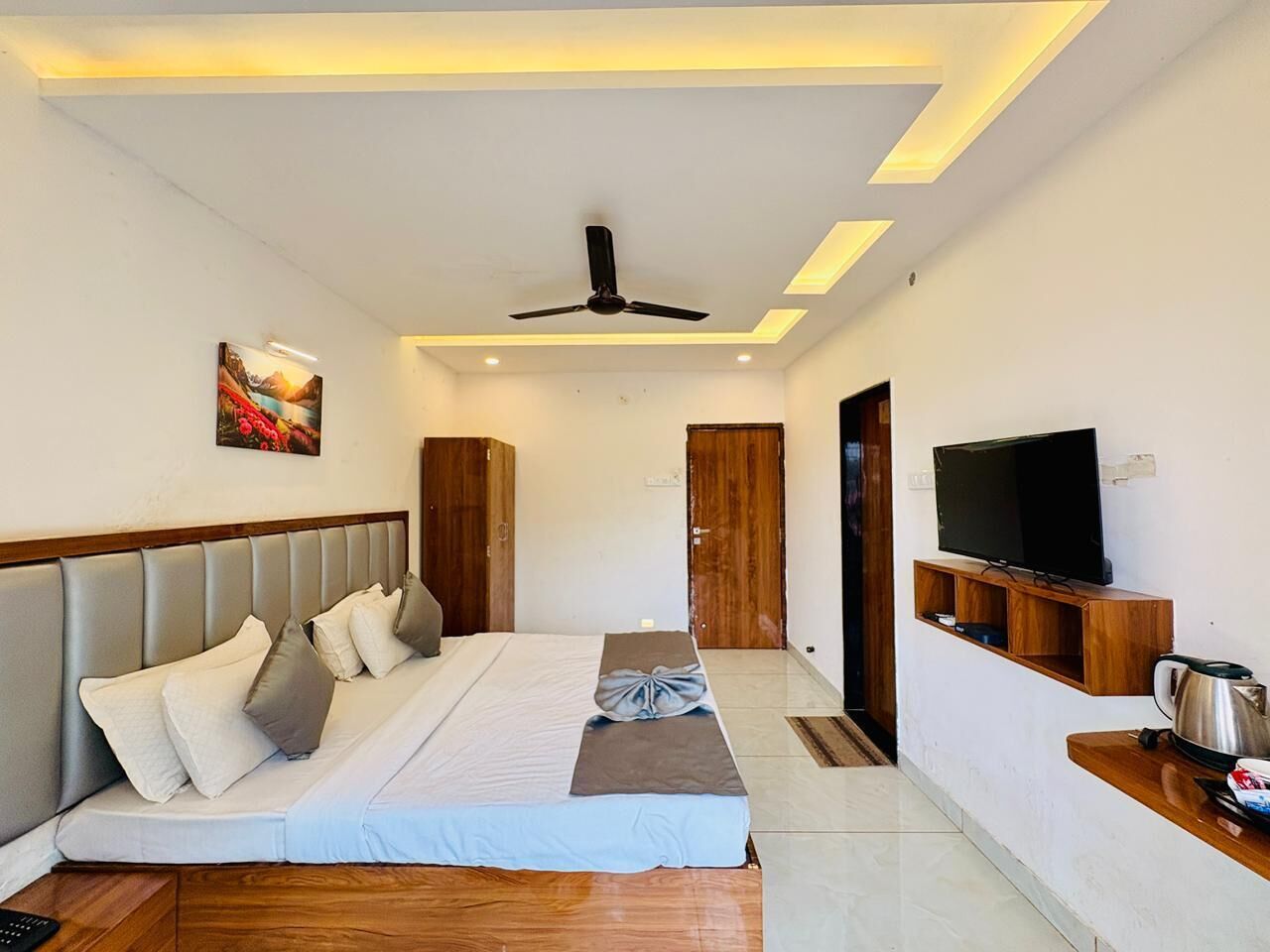 A modern hotel room with a large bed, a ceiling fan, a flat-screen TV, and a wooden coffee table.