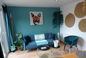 A modern living room with a teal wall, a blue sofa, a coffee table, and a decorative plant.