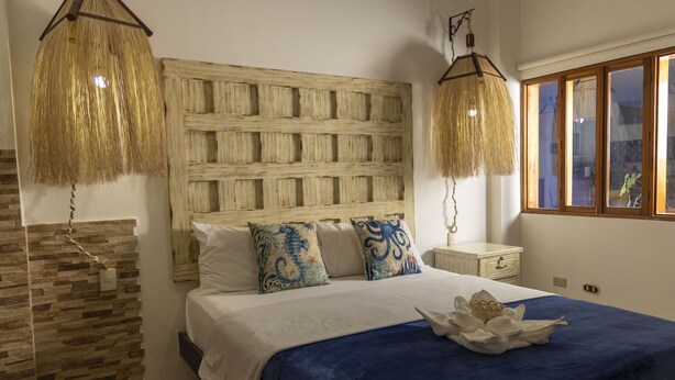 A bedroom with a large bed, a woven headboard, and two hanging lamps.