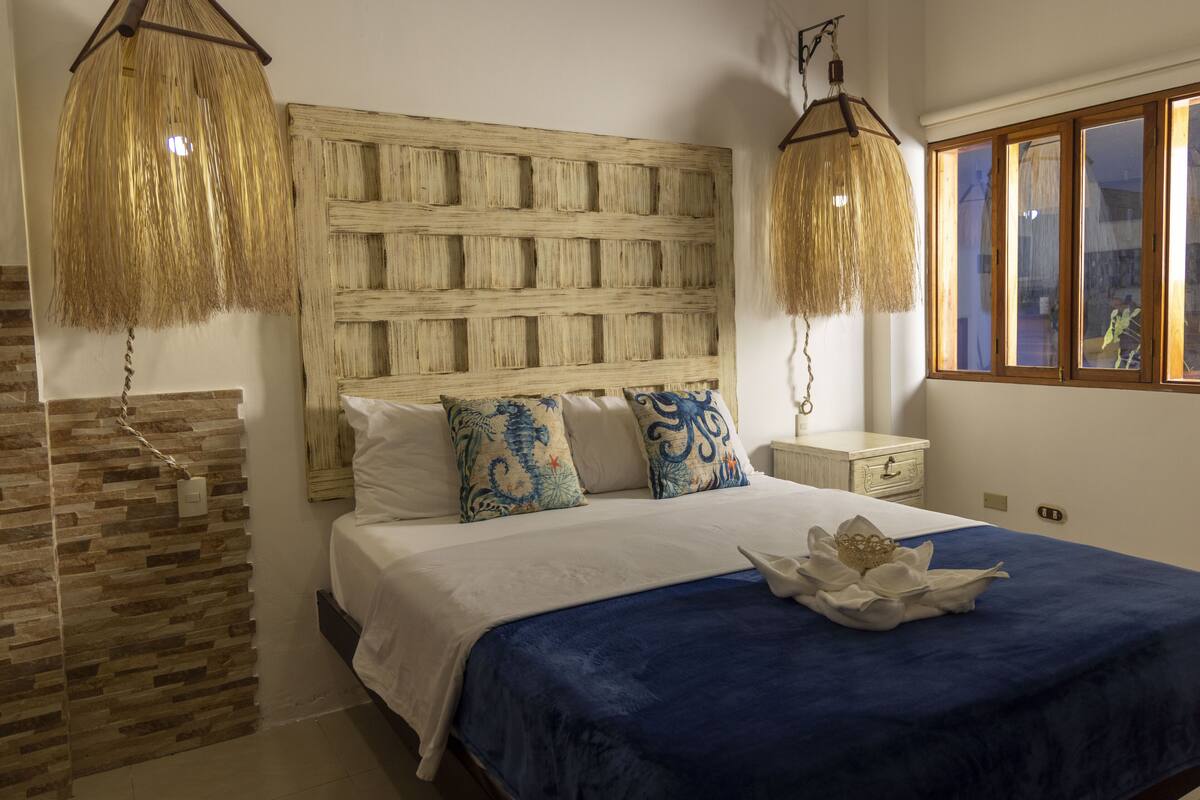 Een slaapkamer met een groot bed, een geweven hoofdbord en twee hanglampen.