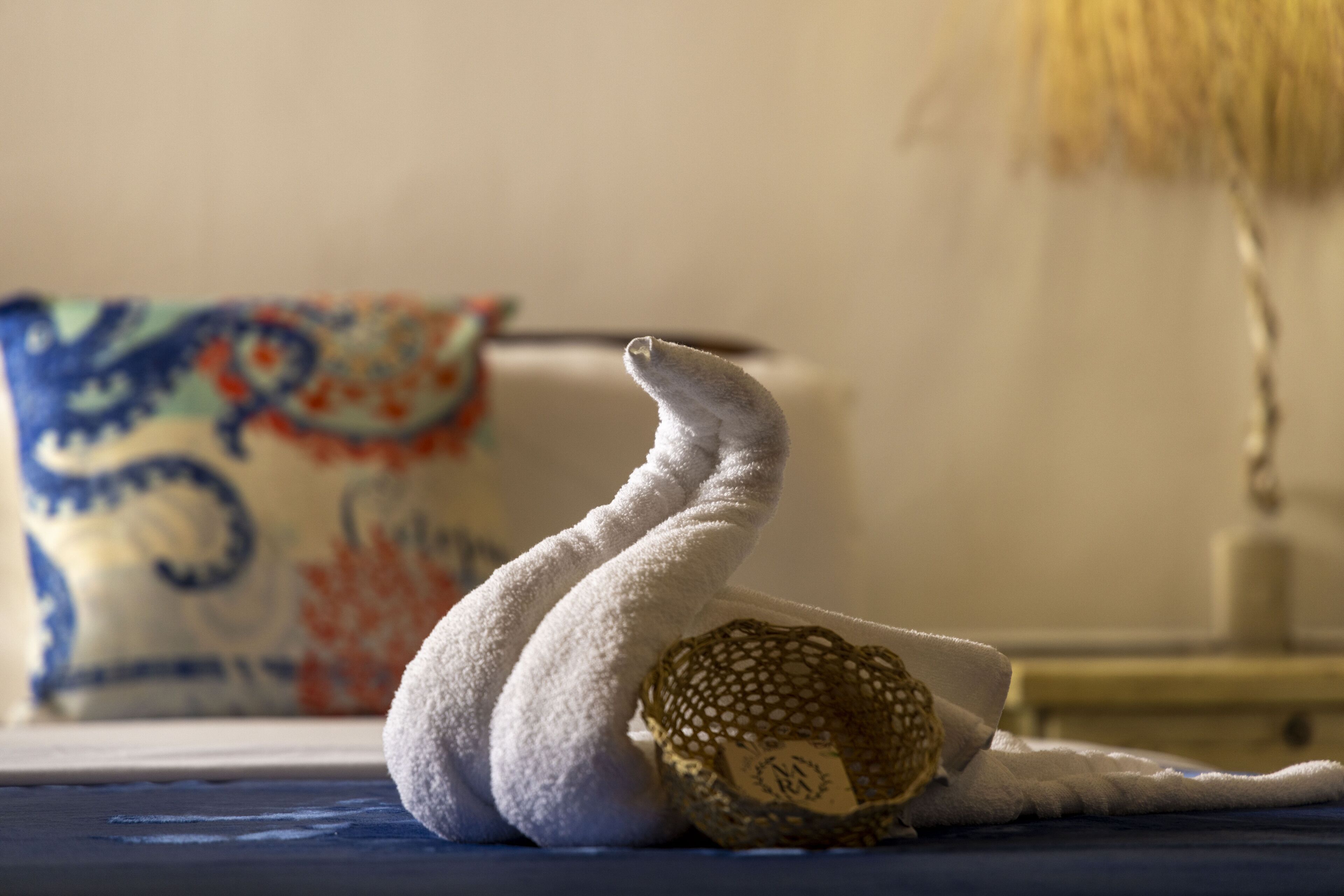 Una toalla doblada con cuidado sobre una cama, con un cojín estampado al fondo.