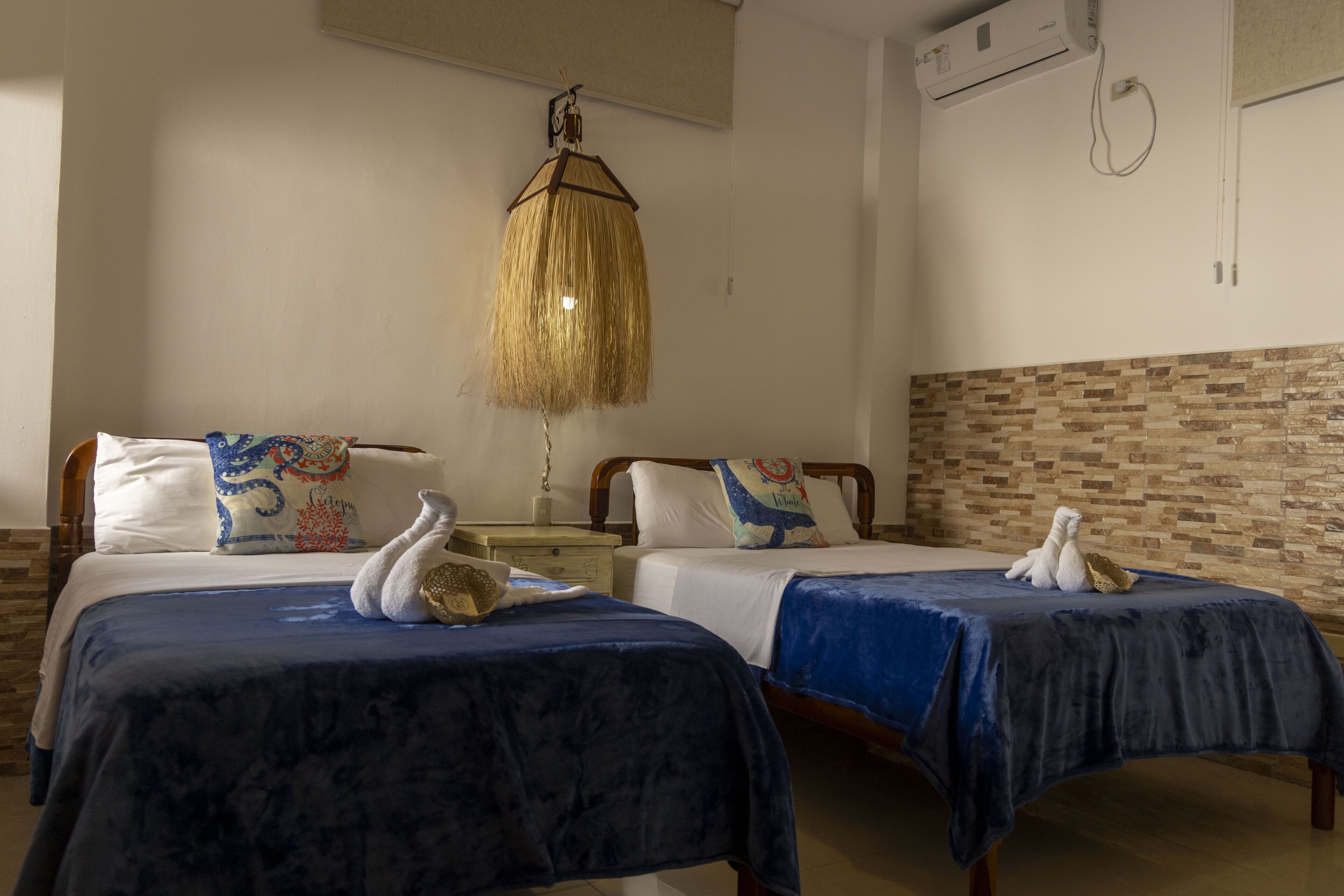 Habitación de hotel con dos camas, una lámpara colgante y pared con diseño de ladrillo.