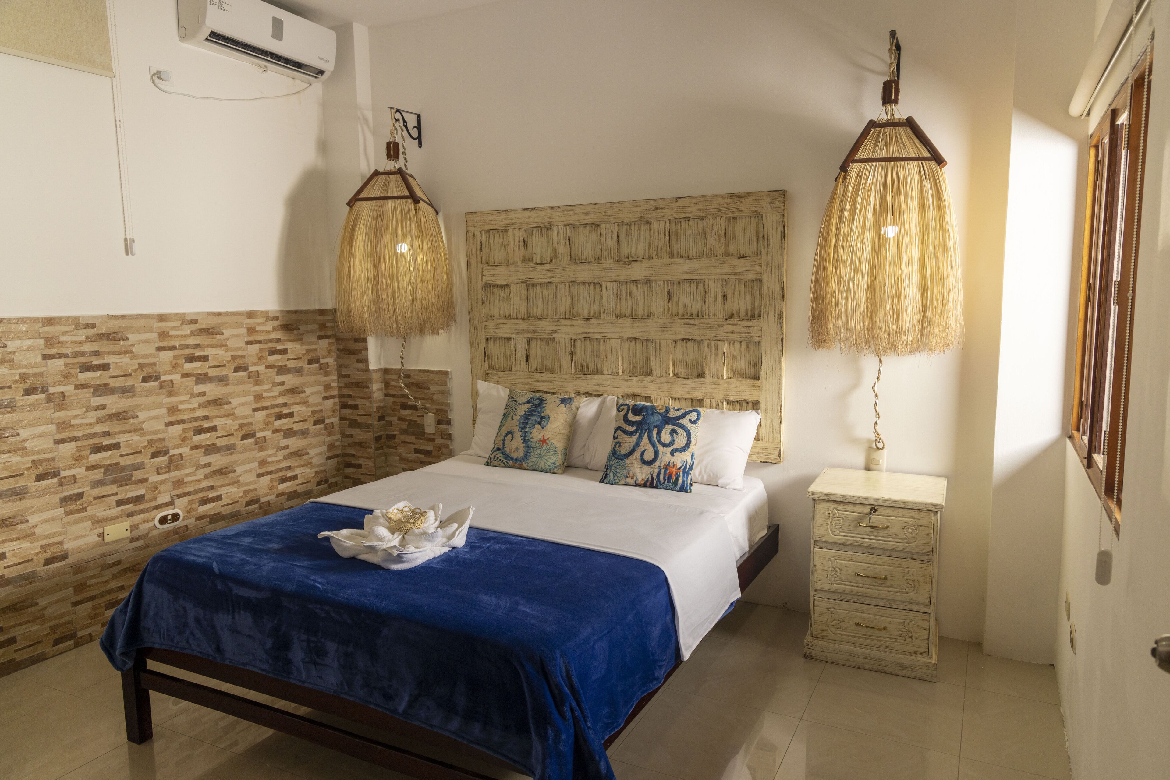 A bedroom with a large bed, a wooden headboard, a bedside table, and a wall-mounted air conditioner.